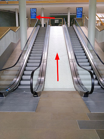 Haupteingang, (Roll-) Treppe hoch in das 1. OG, geradeaus bis nach hinten ins Atrium laufen, dabei den Blick auf die linke Seite halten => Glastür: GLT