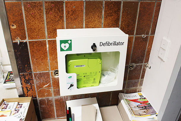 AED Gerät / Defibrillator, befindet sich hinter der Tür im Raum, auf der rechten Seite